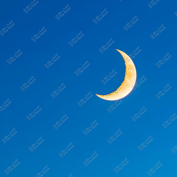 An image showing a bright yellow crescent moon in a clear blue sky. The moon features detailed and visible terrain on its surface.