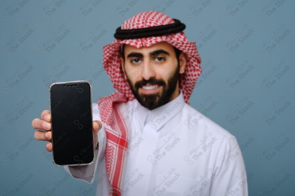 بورتريه شاب سعودي يرتدي الزي السعودي يشير إلى هاتفه ويتفاعل معه، وتظهر على ملامحه الدهشة ، على خلفية سماويه