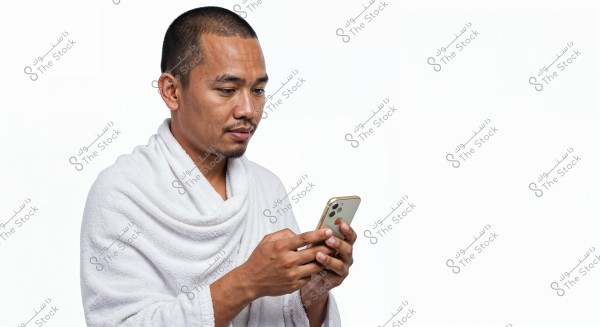 A portrait of a man looking at a mobile phone, wearing a white bathrobe. The man has short hair and is set against a white background, focusing intently on the phone screen. The attire suggests a relaxing moment, possibly at home or after a shower.