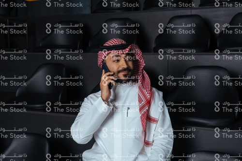 بورتريه رجل سعودي يرتدي الثوب ويجلس على مدرجات سوداء ويتحدث بالهاتف