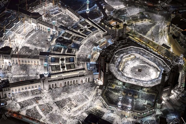 Aerial night view of the Grand Mosque in Mecca, Saudi Arabia, showing the Kaaba surrounded by thousands of worshippers in the mosque\'s courtyards.