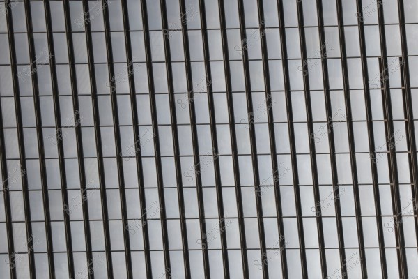 Glass facade of a large building featuring a series of vertical square glass panels, framed with dark metal. Some of the panels gently reflect light, adding a subtle shine.