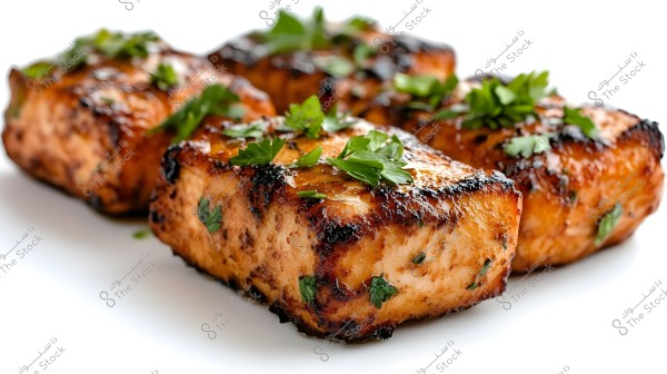 Image of grilled salmon pieces topped with fresh parsley. The salmon has a golden-brown color with visible grill marks, giving it an appetizing and appealing appearance.