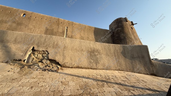 An old brick wall with visible erosion and debris under the morning sun.