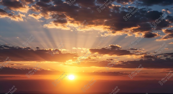 Image of a sunset with the sun nearing the horizon. Golden rays pierce through scattered clouds in the sky, creating a stunning natural scene. The clouds appear in dark and light hues, reflecting the colors of the sunset horizon.