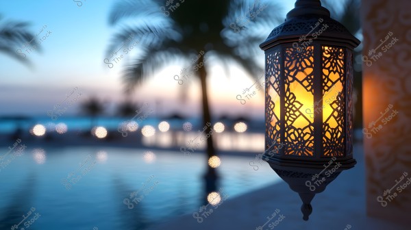A decorative metal lantern illuminated with warm light, hanging against a blurred background of a sea or pool scene at sunset. Some palm trees are visible in the background with lights sparkling like stars, creating a tranquil and beautiful atmosphere.