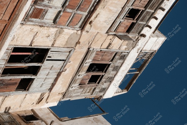 An old building with a deteriorating facade and broken wooden windows, set against a clear blue sky.