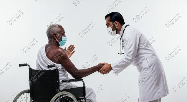 The image shows an elderly man seated in a wheelchair, wearing the Ihram clothing and a blue medical face mask. He is interacting with a doctor dressed in a white coat and face mask, who is bending over and gently shaking the patient\'s hand.