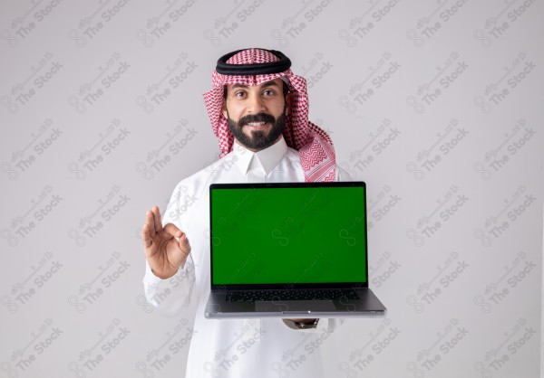 Portrait of a Saudi man holding a laptop, pointing at the laptop and making different expressions - green screen