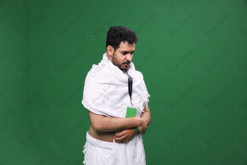 Portrait of a Saudi pilgrim on a green background wearing the Ihram to perform the Hajj rituals during prayer in several directions