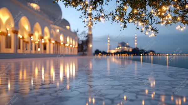 Night view of a mosque illuminated with warm golden lights. The arched columns are seen in sequence on the left, with reflections on the marble floor. A tree on the right is adorned with small lights. In the background, another mosque is visible across the water.