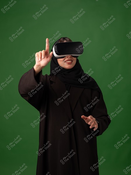 A woman wearing virtual reality goggles on a green background, raising her hand as if interacting with a virtual environment.