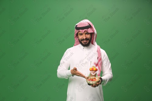 بورتريه رجل سعودي يرتدي الزي السعودي التقليدي يحمل سلة حلويات ويشير إليها