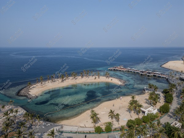 Aerial view of a circular beach surrounded by palm trees and clear blue water in Jeddah.