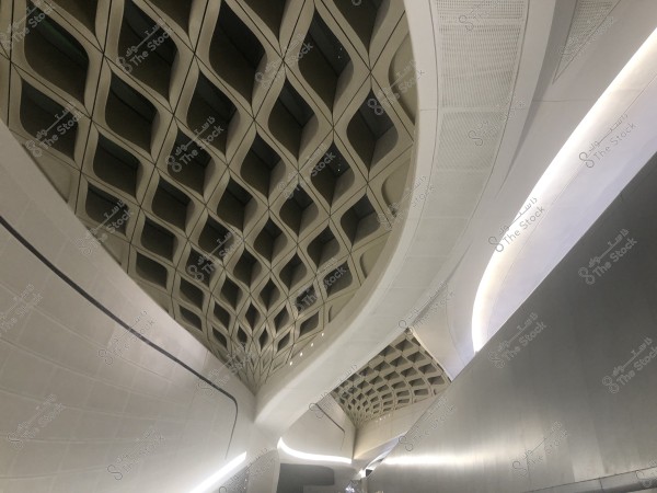 صورة لجزء داخلي من مبنى حديث, تُظهر سقفًا بتصميم هندسي معقد يتكون من نمط شبكي ثلاثي الأبعاد. الإضاءة مخفية وتضفي لمسة أنيقة وحديثة على المساحة.