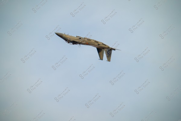 A gray fighter jet flying in the sky, showing detailed features of the wings and tail. The jet appears to be in a roll or aerial maneuver, set against a backdrop of clear blue sky.