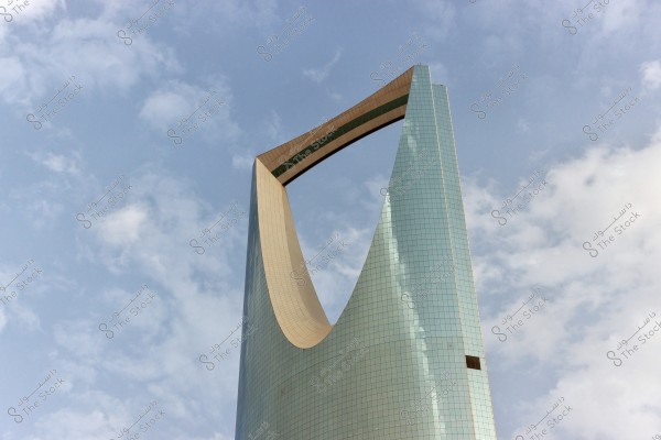 The image shows a famous skyscraper in Riyadh, Saudi Arabia, known as the Kingdom Tower. The tower is distinguished by its unique design resembling a large arch-like opening at the top. The background has a blue sky with some light white clouds.