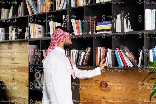 رجل سعودي يرتدي الزي السعودي التقليدي يختار أحد الكتب في المكتبة