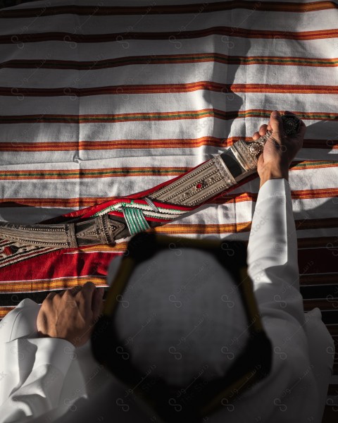 A snapshot of a Saudi man wearing a popular heritage costume on the day of the foundation stands in front of an clay building and puts his hand on his southern sides, heritage uniforms, foundation day, old archaeological buildings, southern side