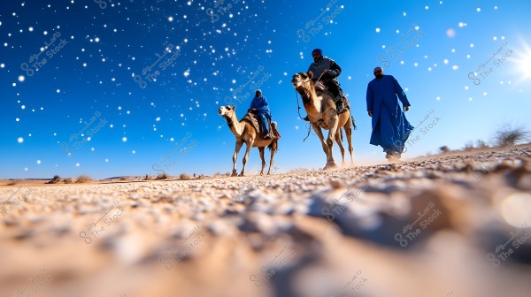 An image of a desert scene featuring three individuals in traditional blue attire, two riding camels and one walking alongside. The sky is clear with bright dots scattered against the blue background. The sun is shining, and the desert ground is covered with small stones.