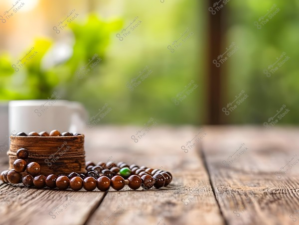 An image of a wooden surface with a brown prayer bead strand wrapped around a small wooden bowl. In the blurred background, there are green plants and a white cup. Natural light creates a serene atmosphere.
