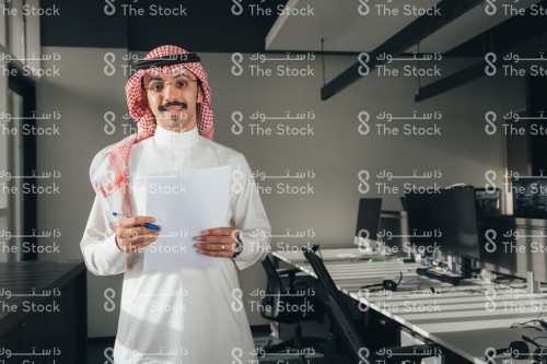 موظف سعودي يرتدي الثوب في العمل ويحمل اوراق بيديه.