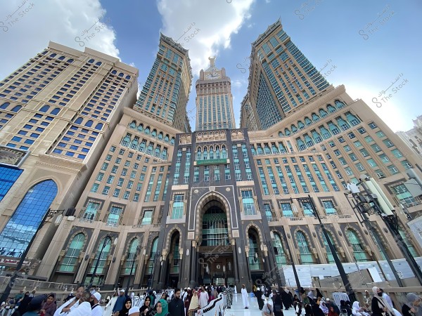 أبراج الساعة في مكة المكرمة تحت سماء صافية مع حشد من الزوار في المقدمة.