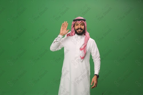 رجل سعودي يقف على خلفية خضراء يرتدي الثوب و الشماغ، يقوم بعمل حركات بيديه يلقي التحية بيده اليمنى، احتفالات العيد