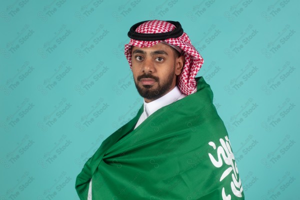 بورتريه رجل سعودي يحمل علم السعودية على كتفه احتفالاً باليوم الوطني على خلفية تركاوزية، احتفالات، اليوم الوطني.