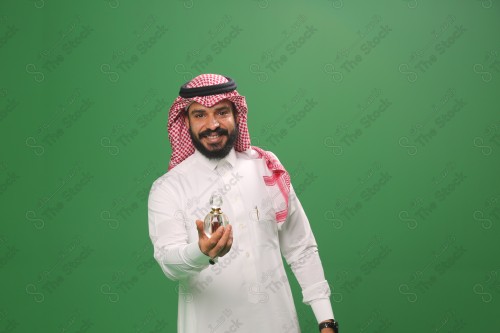 شاب سعودي على خلفية خضراء يرتدي الثوب و الشماغ، يقوم بعمل حركات بيده،يمسك بزجاجة العطر، احتفالات العيد