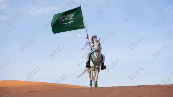 A rider on a white horse in the desert, holding the green Saudi Arabian flag. The rider is dressed in traditional Saudi attire, including a white thobe, ghutra, and agal. The horse is adorned with green and gold decorations.