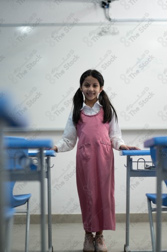 A Saudi student wears a school uniform and does different interactions and shows the tables in the classroom