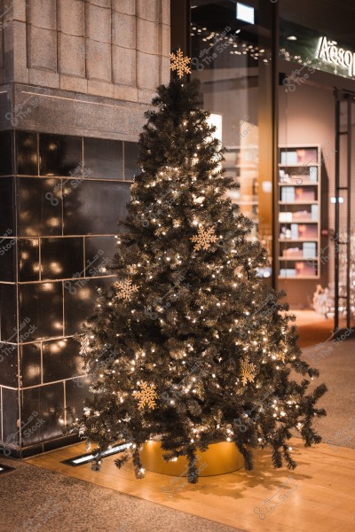 A Christmas tree decorated with white lights and snowflake ornaments, placed inside a store next to a dark wall.