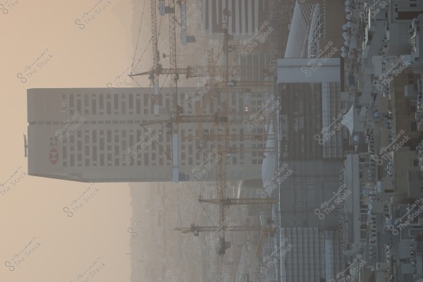 The image shows high-rise buildings in an urban area, with several construction cranes scattered among the buildings. A tall building with a well-known bank logo is prominent, and a haze covers the buildings in the background, conveying a sense of bustling urban development.