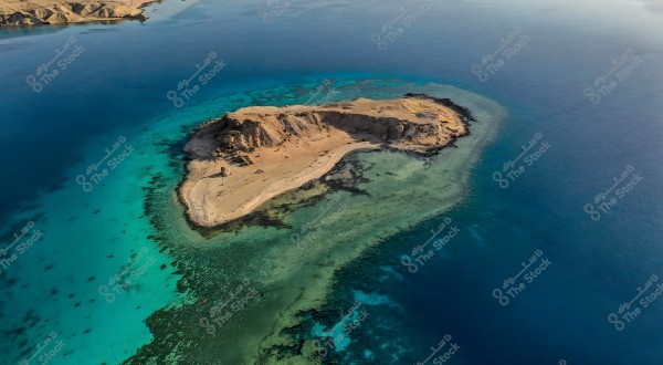 Aerial view of a small island surrounded by clear blue waters with coral reef areas near the coast. The island features brown land with parts of white sand. The turquoise and deep blue water surrounding the island suggests a natural marine area. In the background, part of the shoreline is visible.