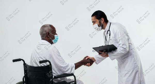 A doctor in a white coat and medical face mask is shaking hands with a patient seated in a wheelchair, wearing a mask and a medical gown. Both are in a medical environment with a white background.
