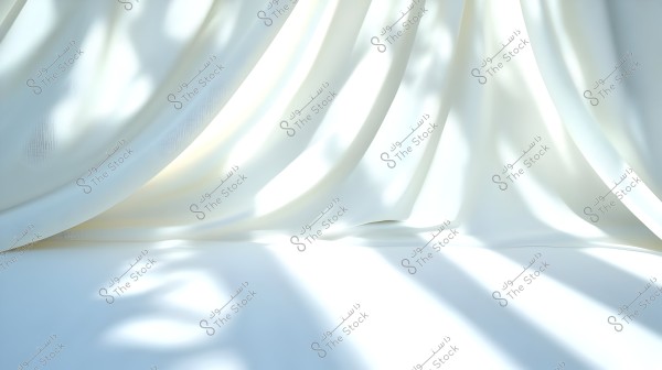 A white curtain drapes smoothly with intermittent light reflections creating a pattern of shadows on the surface beneath it. The image conveys a sense of calm and tranquility due to the light colors and contrast between light and shadow.