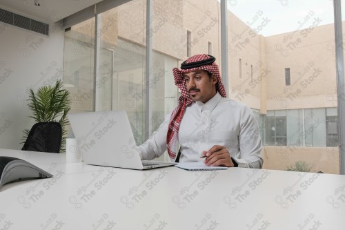 A Saudi man wearing the Saudi thobe sits in the meeting room and uses the mobile device