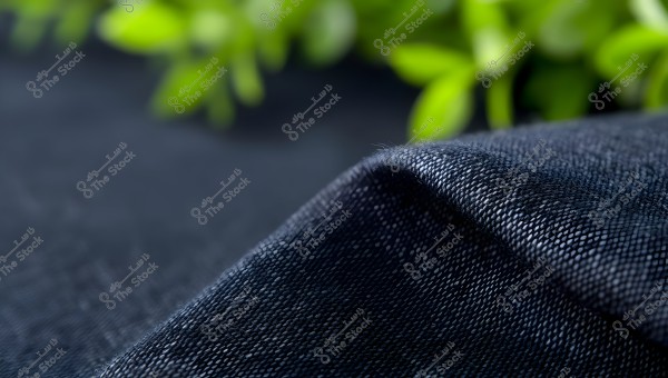 Image of a dark blue fabric draped diagonally in the foreground, with a blurred background featuring green shapes resembling plant leaves.