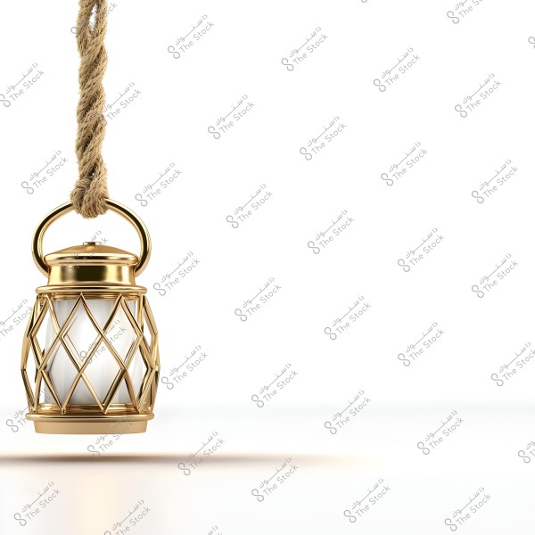 A decorative golden lantern with white glass is hanging from a coarse rope against a white background. The design features a geometric lattice pattern surrounding the glass, suggesting a traditional Arabic style.