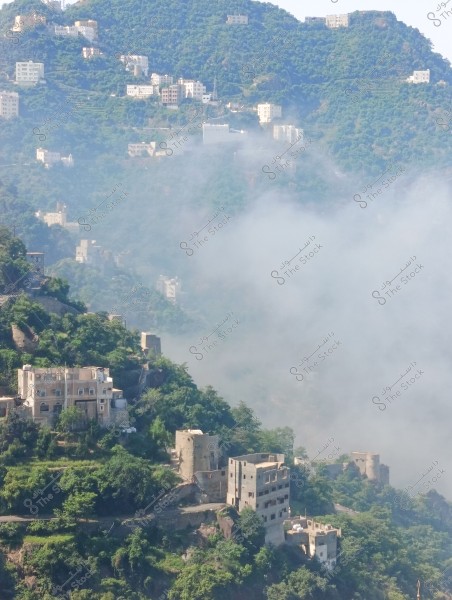 A natural landscape with a mountain covered in greenery, featuring white buildings constructed on the mountain slopes interspersed with clouds. The various elevation buildings are nestled within the dense green nature. The sky is clear, and the weather appears partly cloudy with low clouds covering part of the scene.