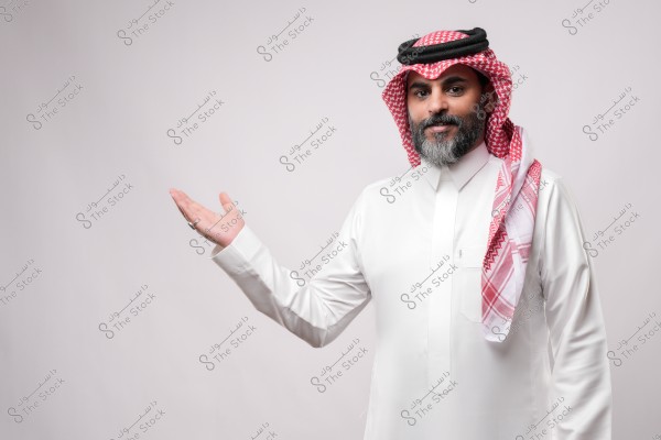 An Arab man wearing traditional Saudi attire, including a thobe, ghutra, and agal, gesturing with his hand in a welcoming manner.