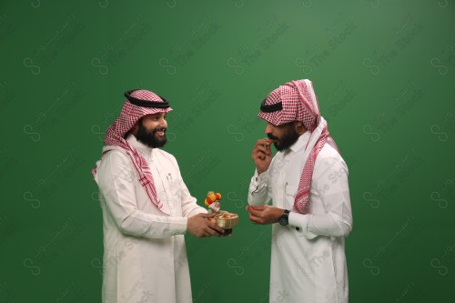 رجل سعودي يرتدي الزي السعودي التقليدي يقدم لضيفه سلة الحلوى في أحد المناسبات