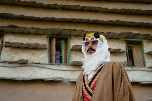 A snapshot of a Saudi man wearing a popular heritage costume on the day of the foundation stands in front of an clay building, heritage uniform, foundation day, old archaeological buildings