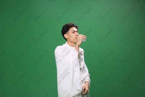 Portrait of a pilgrim with white skin on a green background wearing Ihram drinking water in several directions