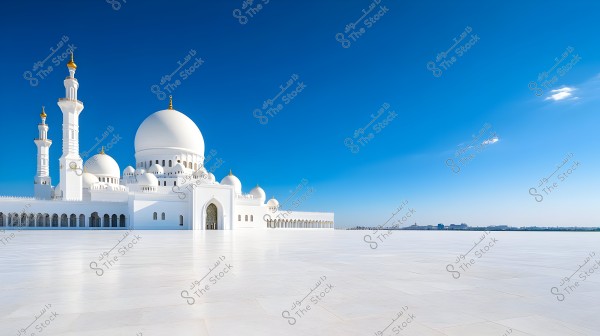 The image shows a large mosque with white domes and tall minarets. The clear blue sky forms a stunning backdrop for the structure. In the foreground, there is an expansive courtyard covered with white tiles, reflecting the magnificent Islamic architecture.