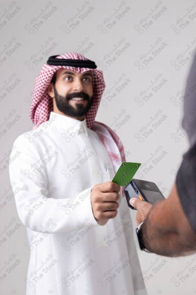 Portrait of a Saudi man holding a card and making automatic payments on a white background