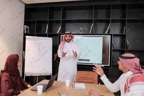 A Saudi man in traditional Saudi dress conducts a business meeting in the boardroom during the day