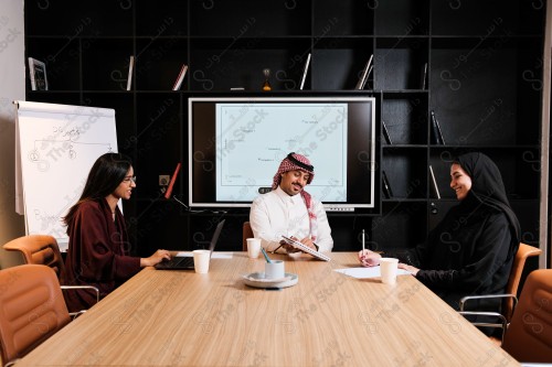 A Saudi man in traditional Saudi dress holds a meeting with Saudi female employees wearing abaya in the meeting room