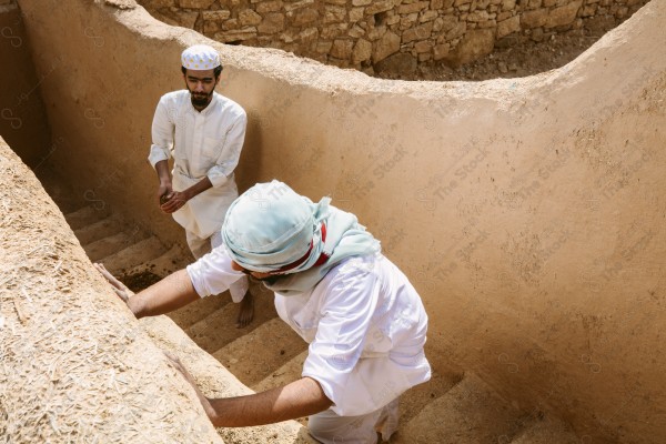 لقطة لرجلان سعوديان يعملان في بناء البيت قديم يرتدون الزي السعودي التقليدي الذي يمثل التراث الشعبي ، يوم التأسيس، الثقافة السعودية